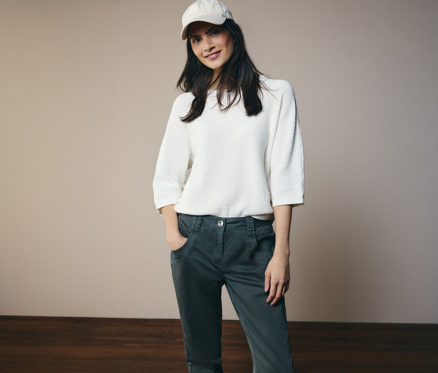 Une femme portant un haut blanc et une casquette pose en pantalon CECIL « Scarlett » avec les mains dans les poches.