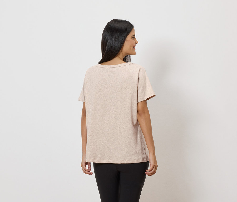 Femme vue de dos portant un t-shirt beige et un legging noir sur fond blanc.
