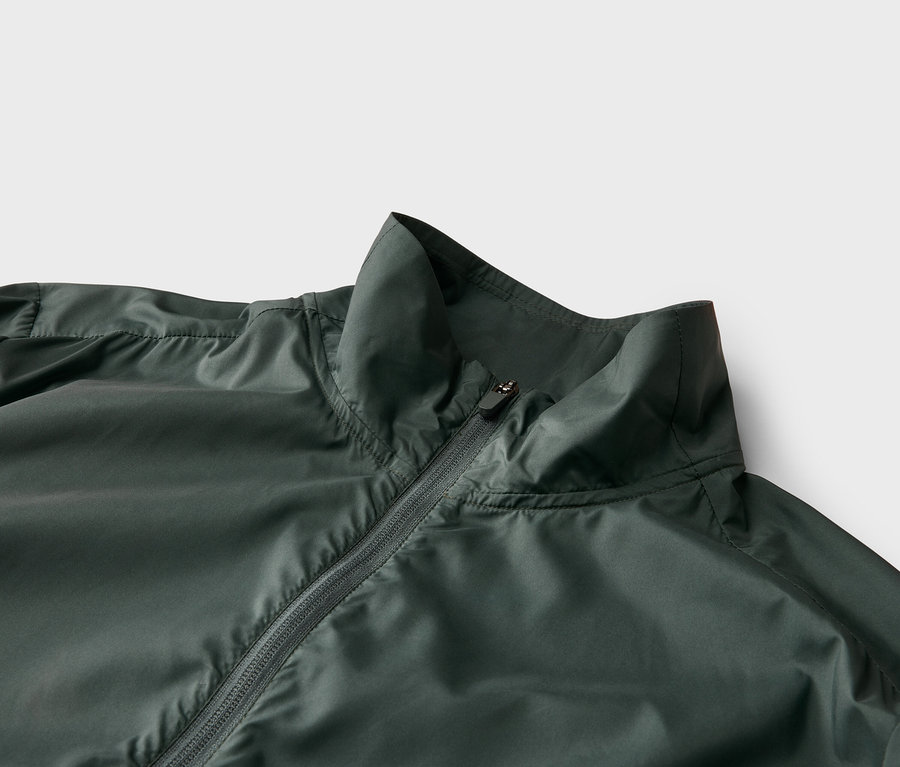 Gros plan d'une veste vert foncé avec fermeture éclair et col montant sur fond clair.