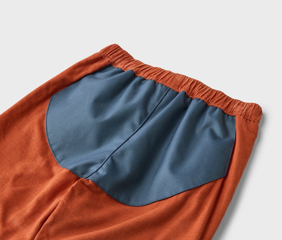 Gros plan d'un pantalon en velours côtelé orange avec un empiècement bleu marine à la taille.