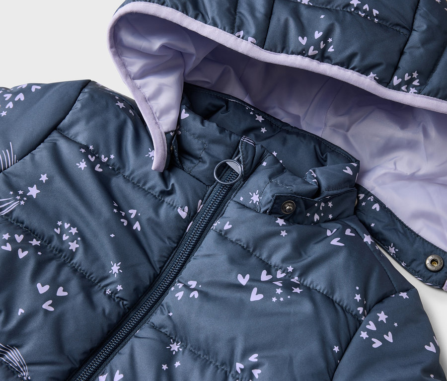 Gros plan d'une veste matelassée bleu marine à capuche et fermeture éclair, ornée de cœurs, d'étoiles et de comètes violets.