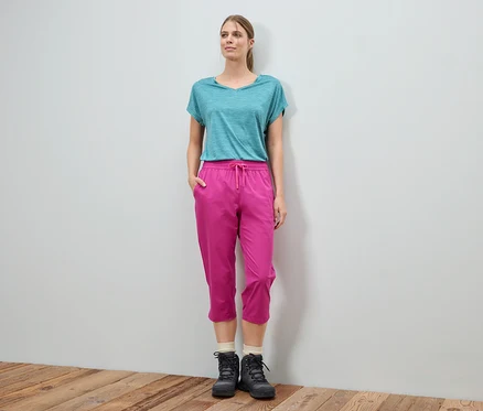 Une femme se tient devant un mur et porte un t-shirt bleu, un pantalon rose et des bottes noires.