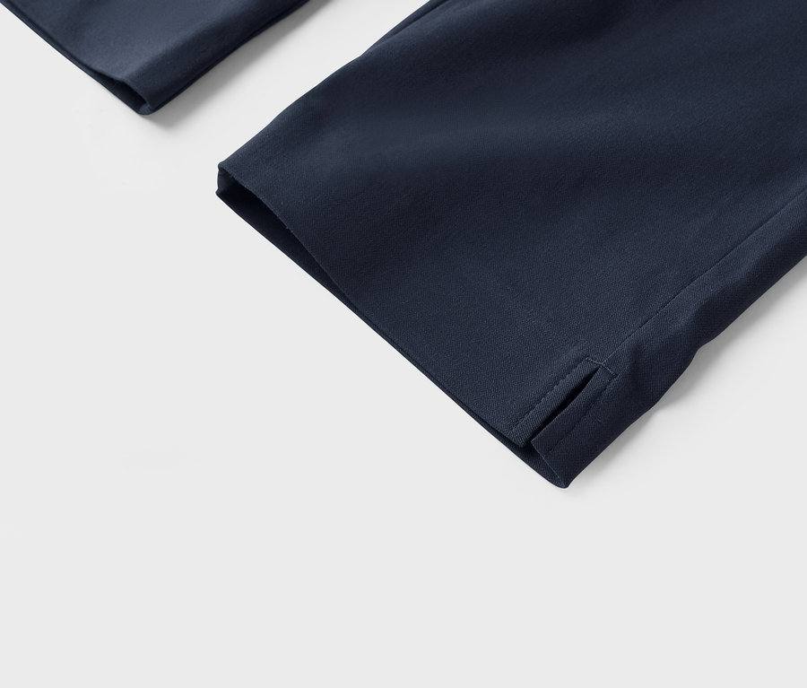 Gros plan sur des jambes de pantalon bleu marine avec une fente à l'ourlet sur fond blanc.