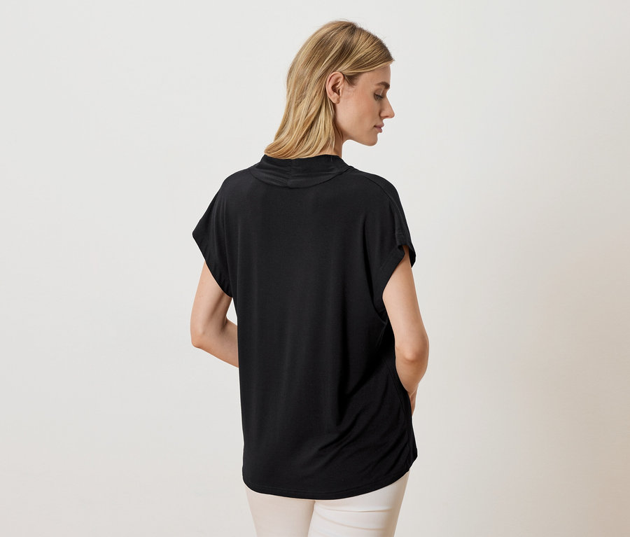 Femme vue de dos portant un haut noir et un pantalon clair.