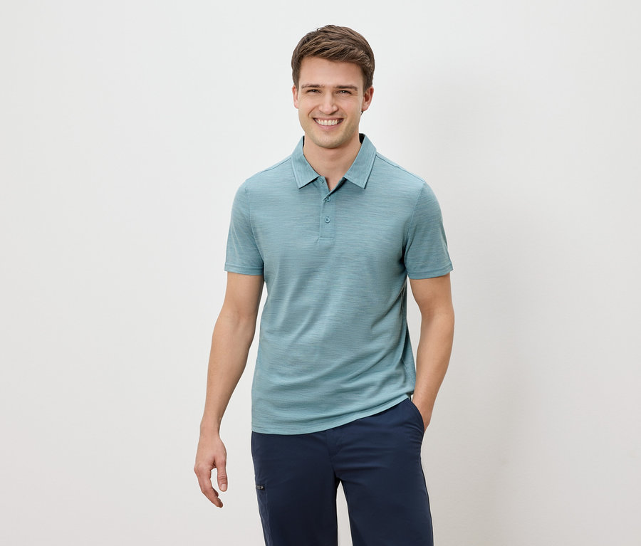 Homme souriant portant un polo bleu et un pantalon bleu marine.