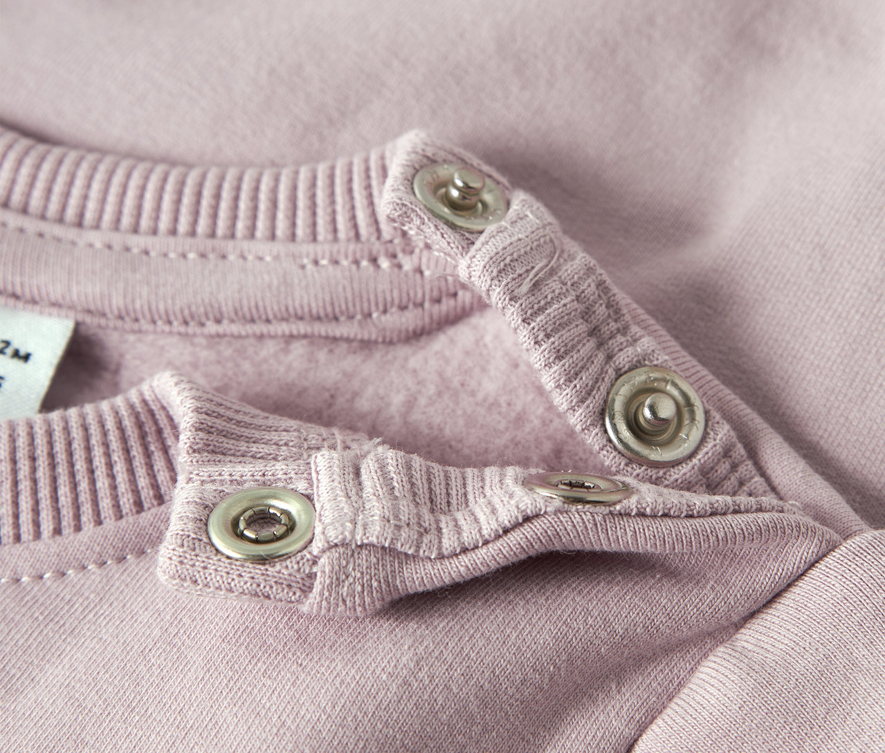 Gros plan sur un sweat-shirt rose NAME IT pour bébé avec des boutons-pression au niveau du col.