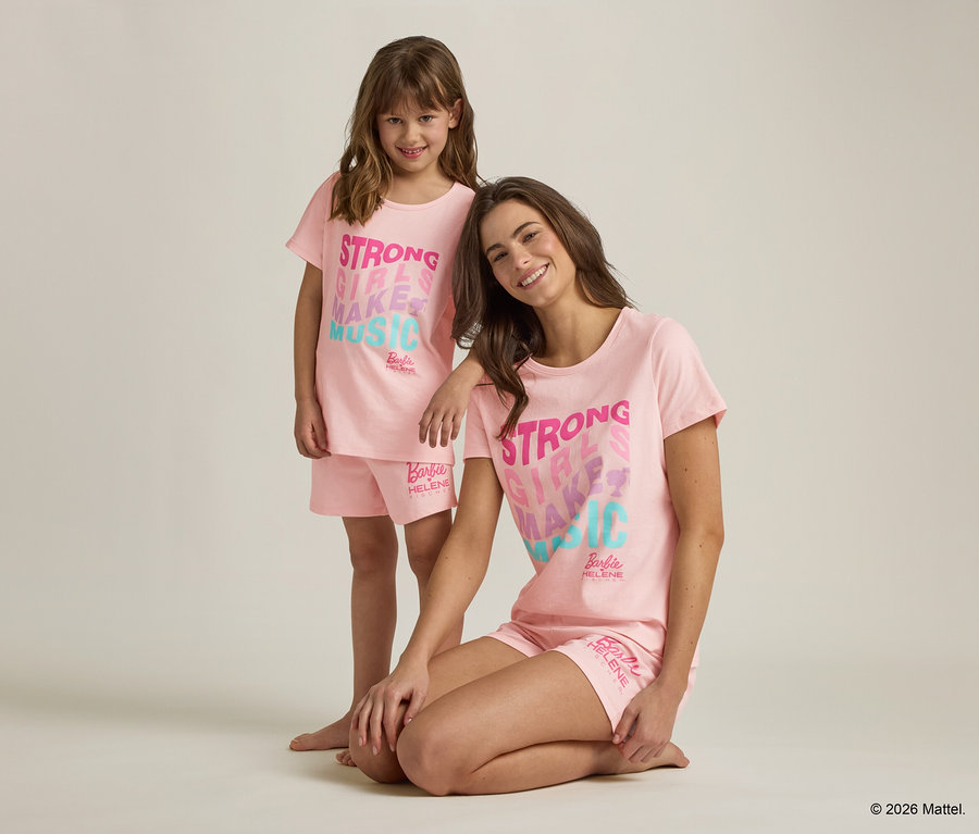 Une jeune femme est agenouillée à côté d'une fille, toutes deux portant des pyjamas roses assortis Barbie avec l'inscription "Strong Girls Make Music".