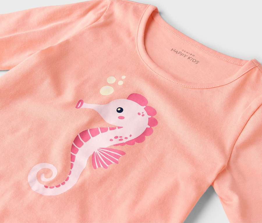 Gros plan d'un t-shirt couleur saumon avec un imprimé hippocampe rose.