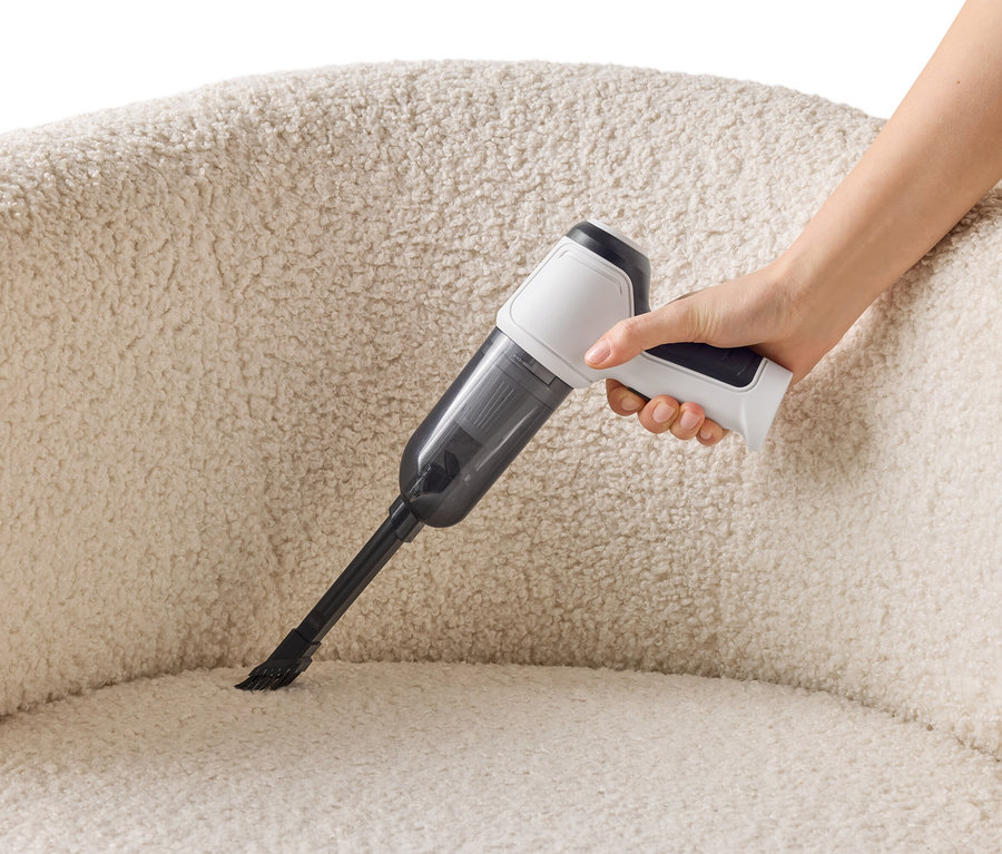 Une main tient un aspirateur sans fil pour nettoyer un fauteuil crème.