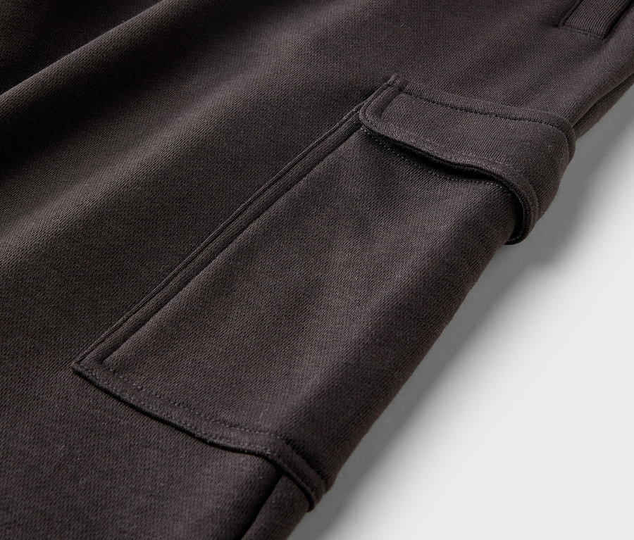 Gros plan d'un pantalon cargo marron avec une poche plaquée et une fermeture boutonnée sur fond blanc.
