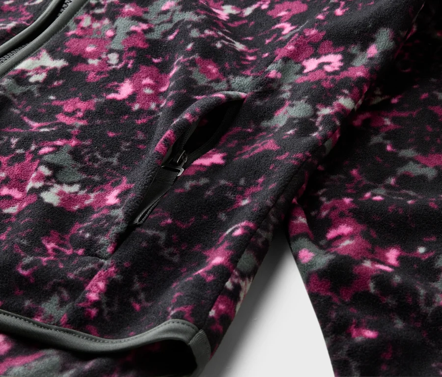Gros plan d'une veste polaire zippée avec un motif rose, gris et noir. Une poche zippée est visible.