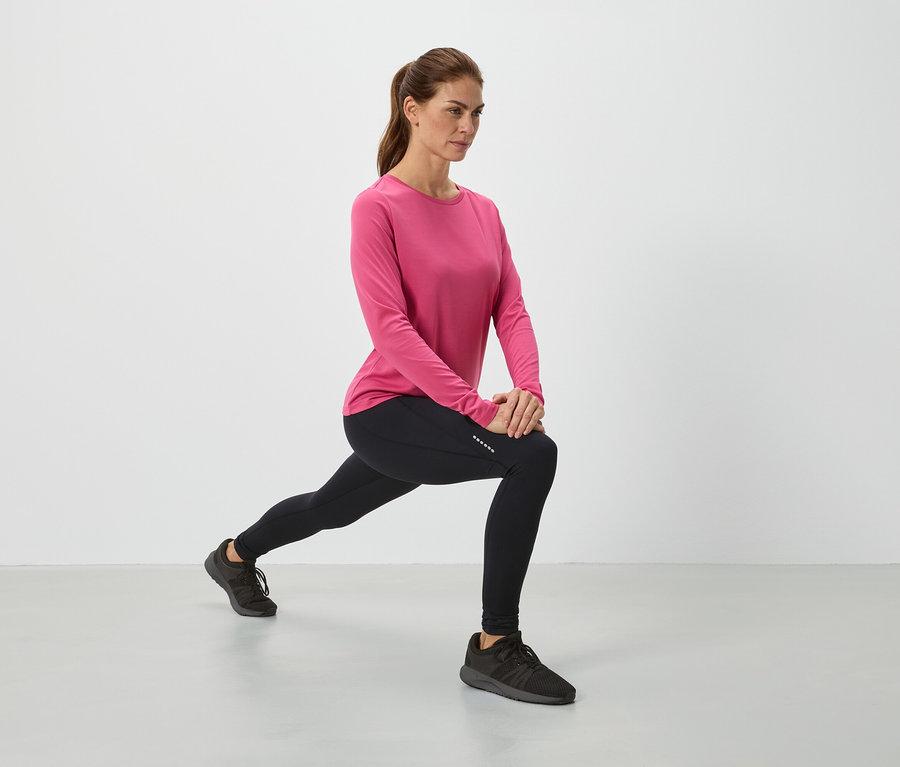 Femme en haut rose et leggings noirs en train de s'étirer.