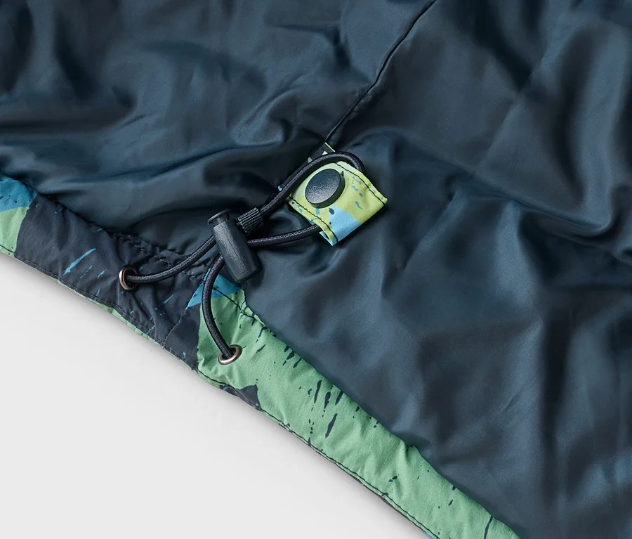 Gros plan d'une veste bleu-vert foncé avec une bordure à motifs verts et bleus. Un cordon de serrage noir avec un stoppeur et un bouton-pression noir sont visibles.