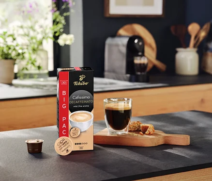 Sur un comptoir de cuisine se trouvent un paquet de capsules Cafissimo Decaffeinato, une tasse de café et une capsule.