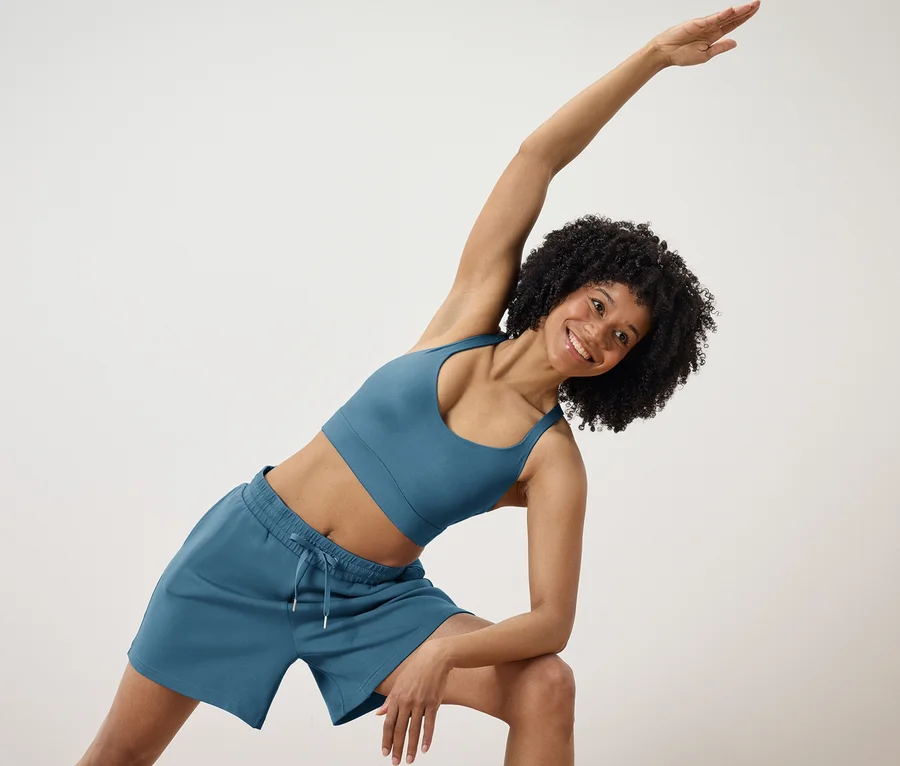 Femme aux cheveux bouclés posant en soutien-gorge de sport et short bleus.