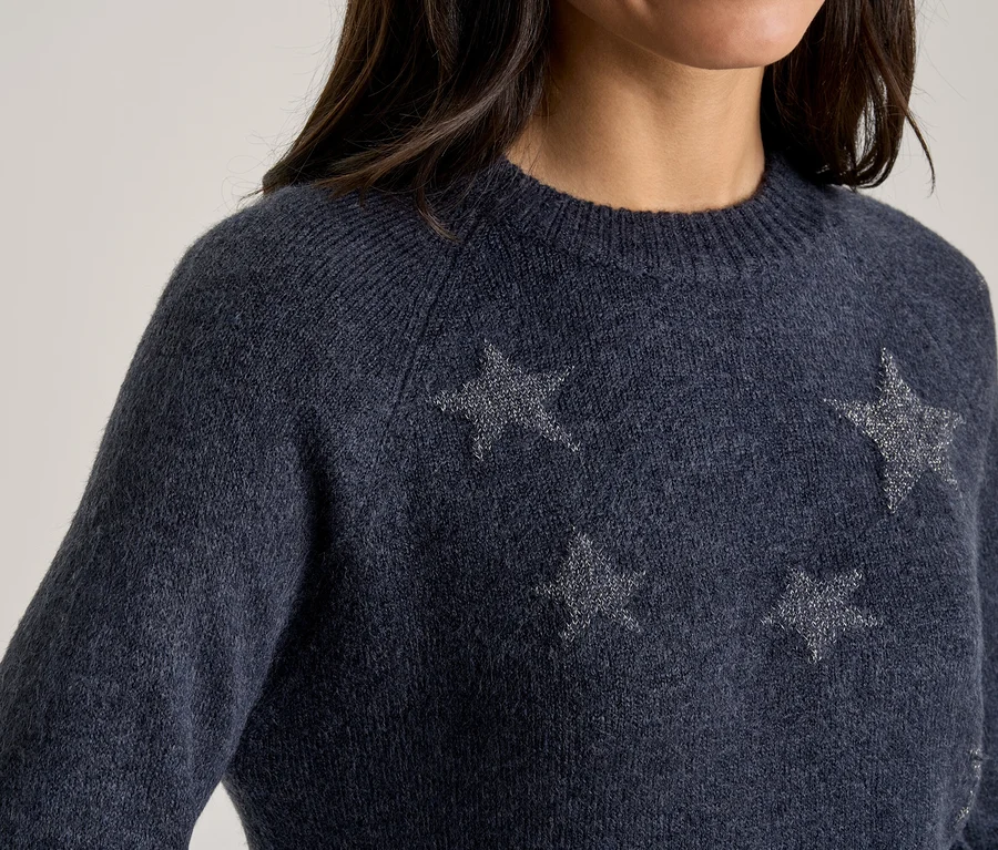 Gros plan sur une personne portant un pull en maille bleu foncé orné d'étoiles scintillantes argentées.
