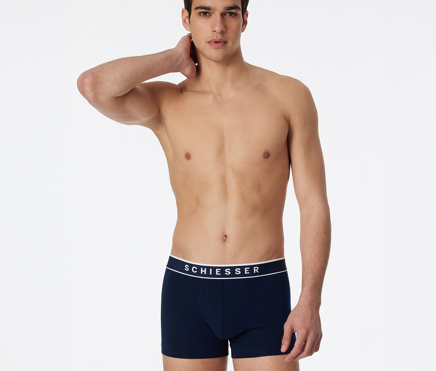 Homme torse nu, la main droite derrière la nuque, portant un short SCHIESSER bleu foncé avec une ceinture blanche.
