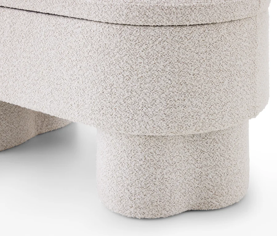 Gros plan d'un pouf ou tabouret en bouclé texturé beige clair, aux formes arrondies et organiques, avec une base empilée.