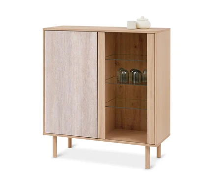 Meuble en bois clair à deux sections; la gauche a une porte fermée avec une surface claire et texturée, la droite a des étagères en verre ouvertes avec trois verres retournés. Une tasse blanche et un pot blanc à couvercle sont posés sur le dessus.