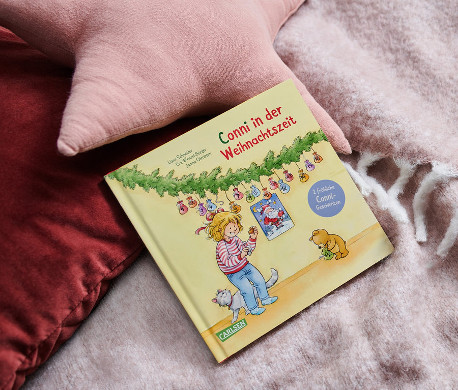 Le livre Conni à Noël est posé sur une couverture à côté de coussins roses.