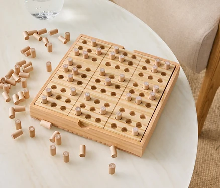 Jeu en bois avec des chevilles sur une table à côté d'un verre d'eau.