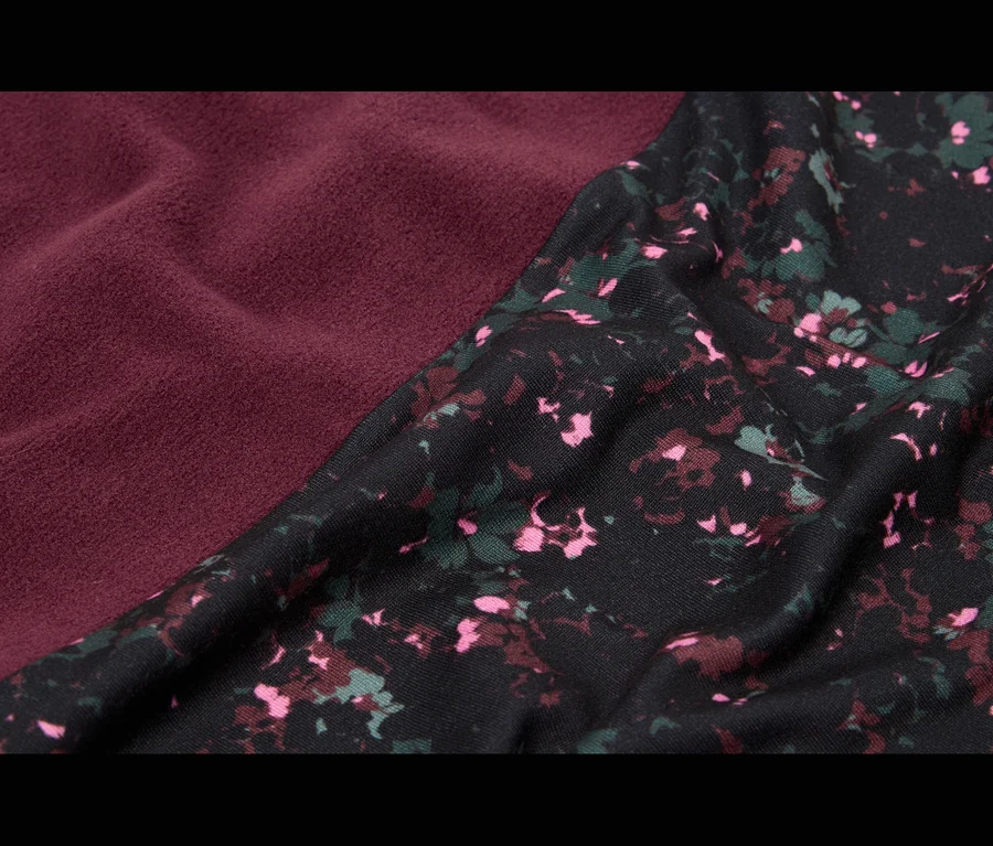 Gros plan de deux tissus se rencontrant en diagonale; l'un est un tissu texturé bordeaux, l'autre est noir avec un motif floral dispersé en rose, rouge foncé et vert.