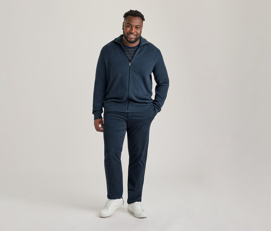 Homme souriant portant un cardigan zippé bleu marine sur un t-shirt rayé et un pantalon chino bleu marine.