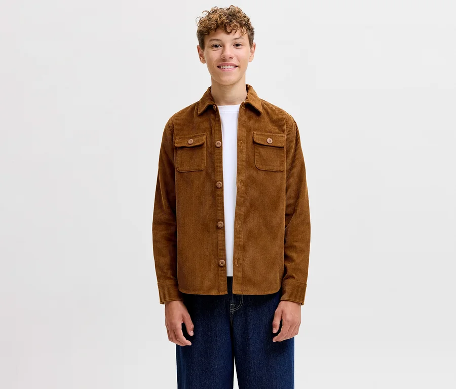 Jeune homme souriant portant une chemise en velours côtelé Jack&Jones Regent marron sur un t-shirt blanc et un jean bleu.