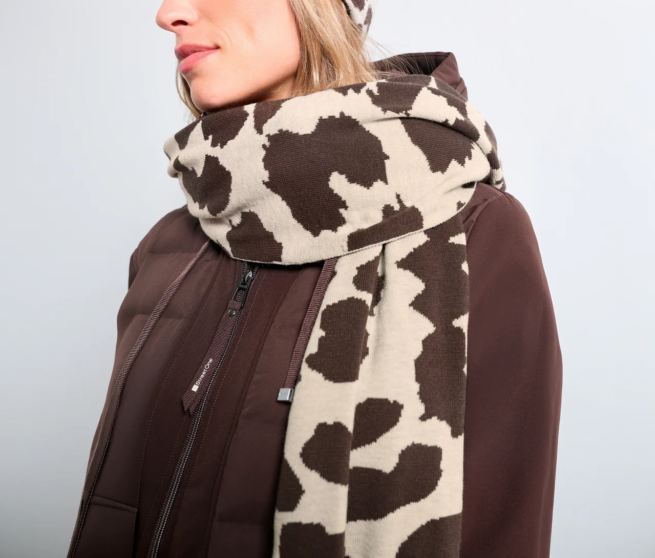 Femme portant une doudoune marron et une écharpe en maille fine Street One à motif animalier marron et beige, avec un bonnet assorti.
