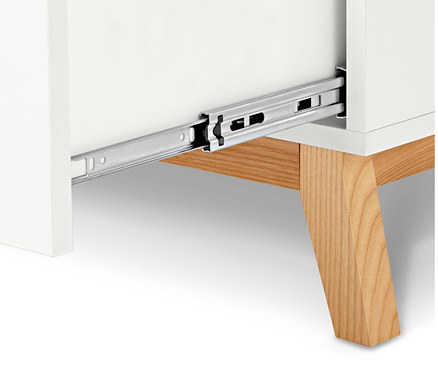 Détail d'une commode blanche avec tiroir ouvert et pieds en bois.