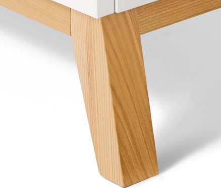 Détail d'une commode blanche avec pieds en bois clair.