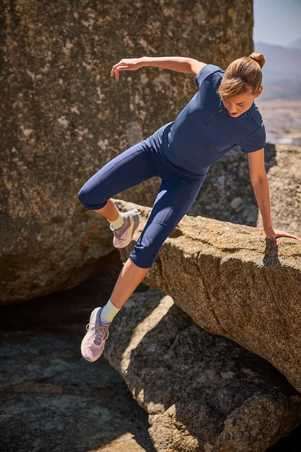 Femme faisant de l'escalade sur des rochers en legging de trekking 3/4 et t-shirt de sport à demi fermeture éclair.
