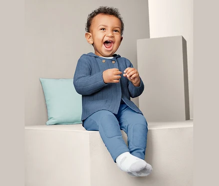 Bébé souriant assis portant une jaquette en maille bleue.