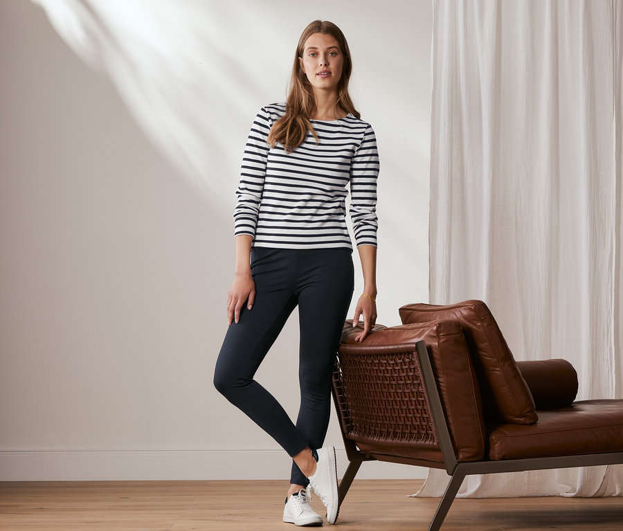 Une femme pose, appuyée contre un canapé en cuir, portant un legging basique en jersey lourd, bleu foncé.