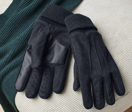 Sur un tabouret beige reposent une paire de gants noirs et un pull vert.