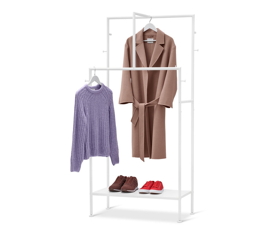 Un portemanteau blanc avec un pull violet et un manteau marron suspendus. Des chaussures marron et rouge sont posées sur l'étagère inférieure.