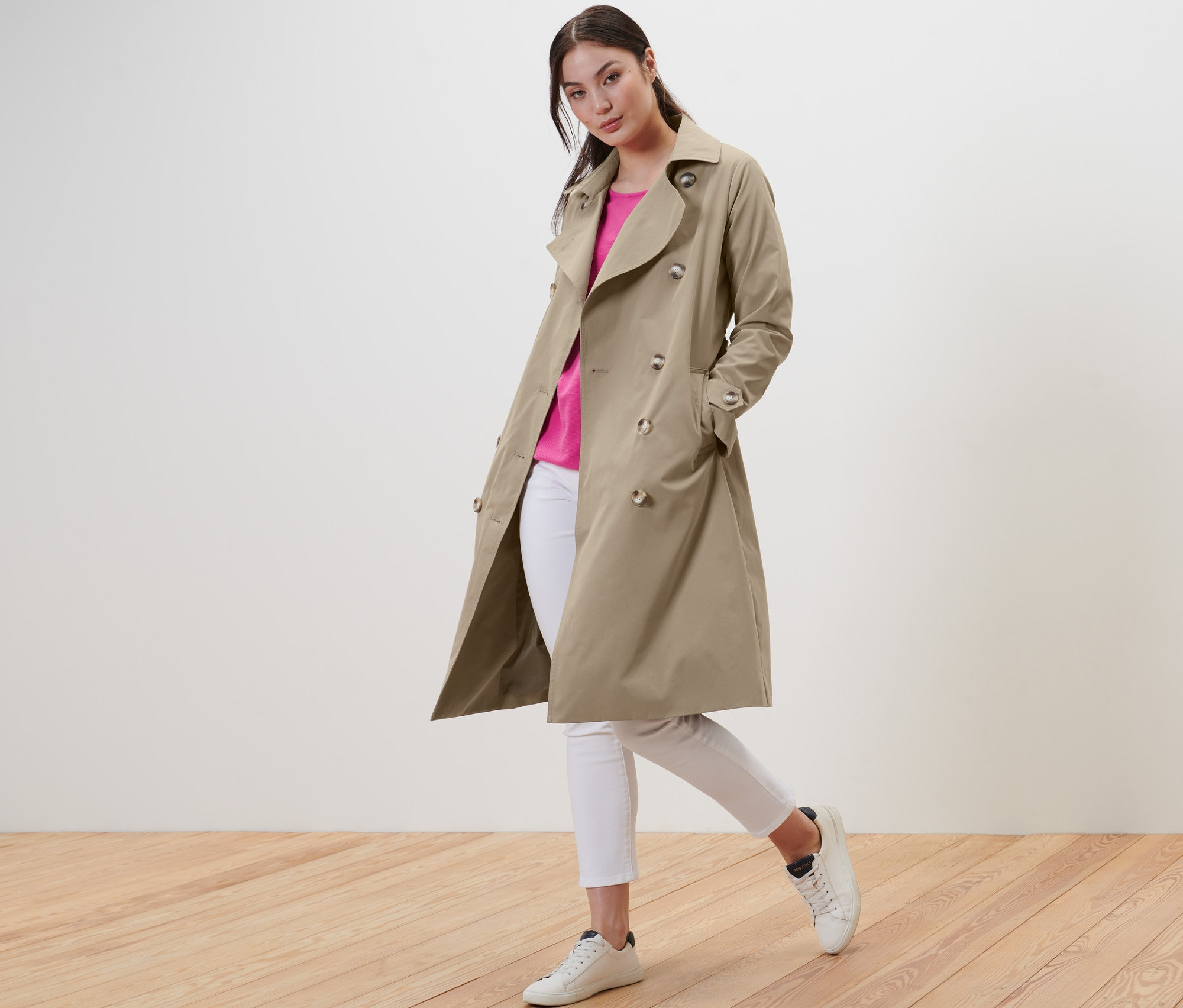 Femme posant en trench beige, jean blanc et baskets.