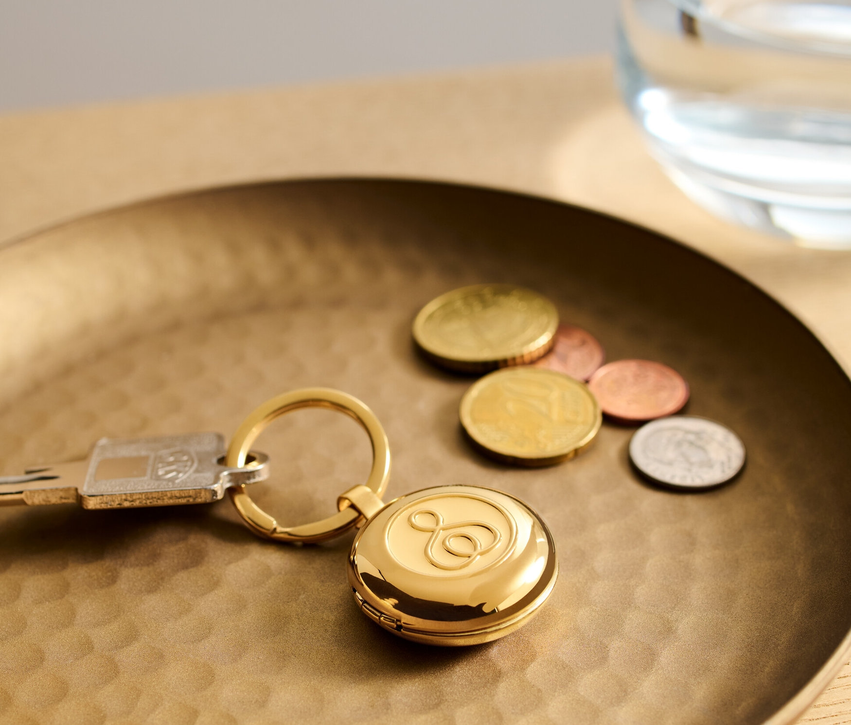 Un porte-clés boîte à pilules doré est posé sur un plateau doré à côté de clés et de pièces de monnaie.