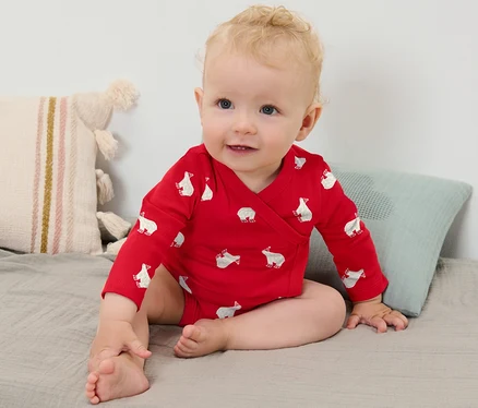 Une petite fille blonde porte un body rouge à manches longues avec un motif d'ours polaire et est assise sur une couverture grise.
