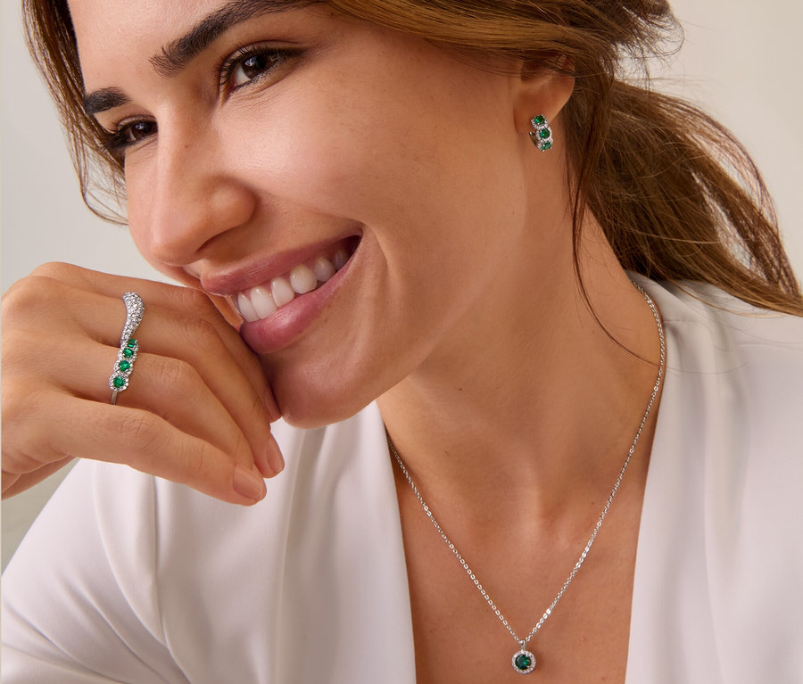Une femme souriante aux cheveux bruns porte des créoles en argent 925, une bague en argent 925, une bague en argent 925 vague et une chaîne en argent 925.