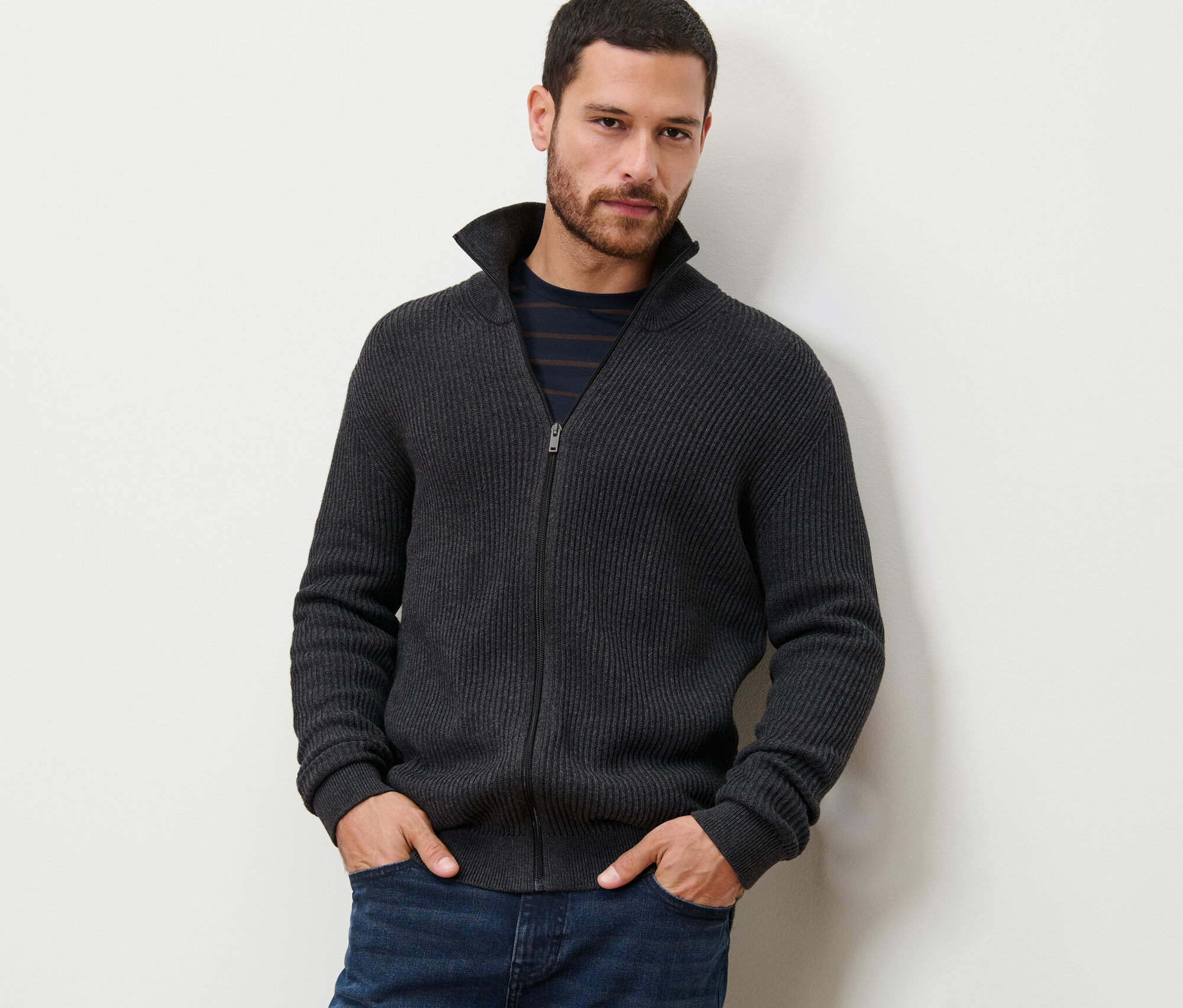 Un homme debout, les mains dans les poches, portant une jaquette en maille anthracite chiné.