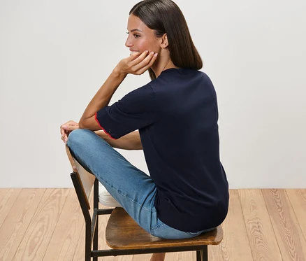 Une femme est assise sur une chaise et porte un pull bleu foncé en maille fine et un jean bleu.