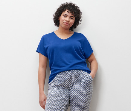 Une femme se tient debout, la main dans la poche d'un pantalon imprimé, portant une chemise bleu cobalt et des baskets en toile.