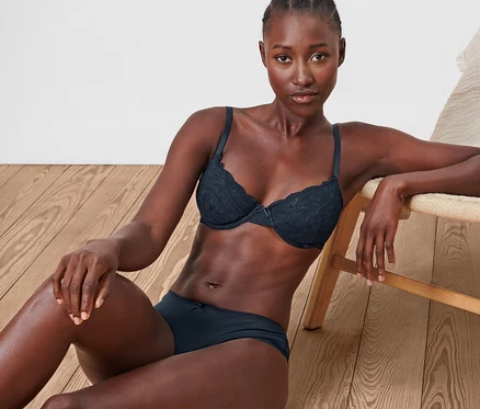 Une femme assise par terre à côté d'une chaise porte un soutien-gorge à armatures bleu en dentelle.
