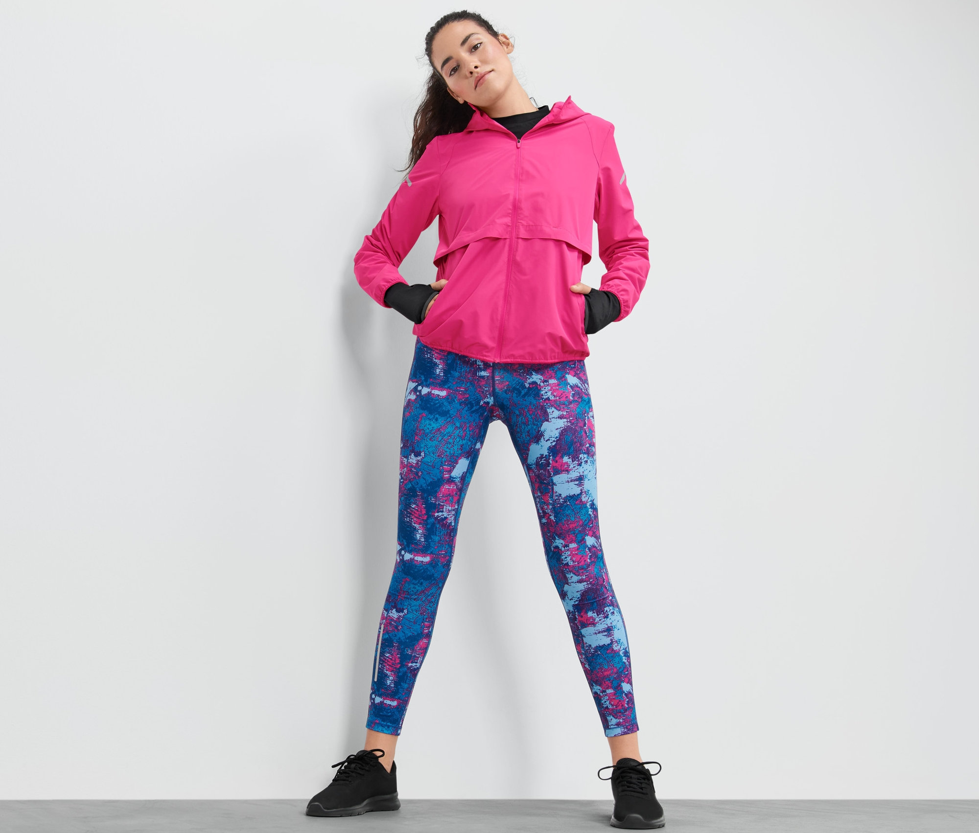 Femme posant en veste de sport coupe-vent rose et leggings à motifs.
