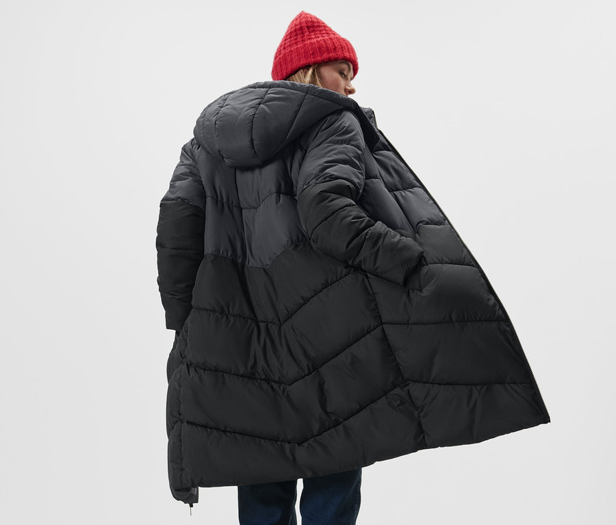 Femme portant un manteau matelassé à capuche et un bonnet rouge.