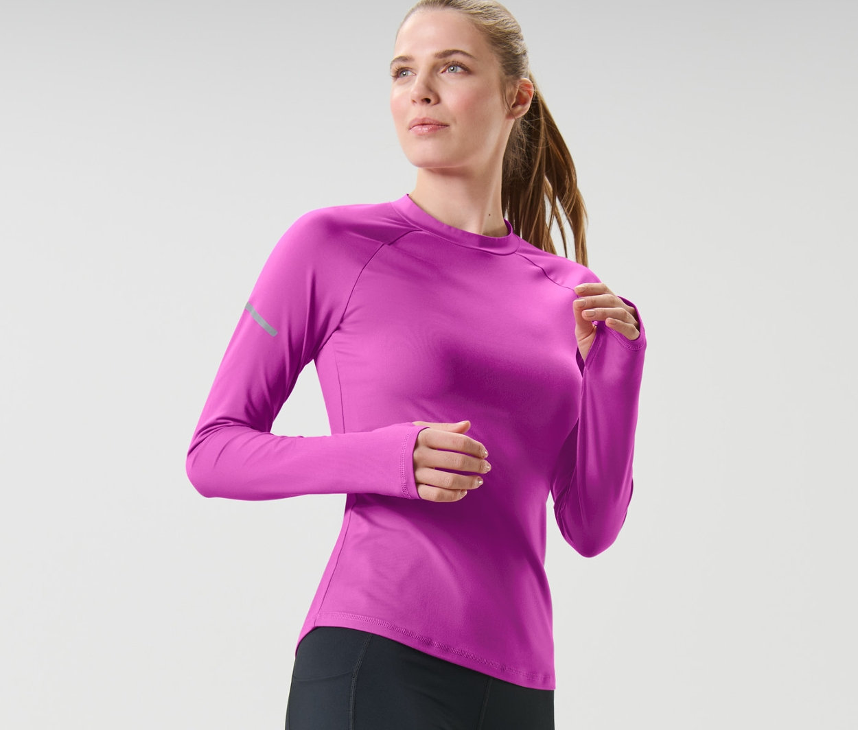 Femme portant des leggings noirs et un t-shirt technique à manches longues rose baie fluo en courant.