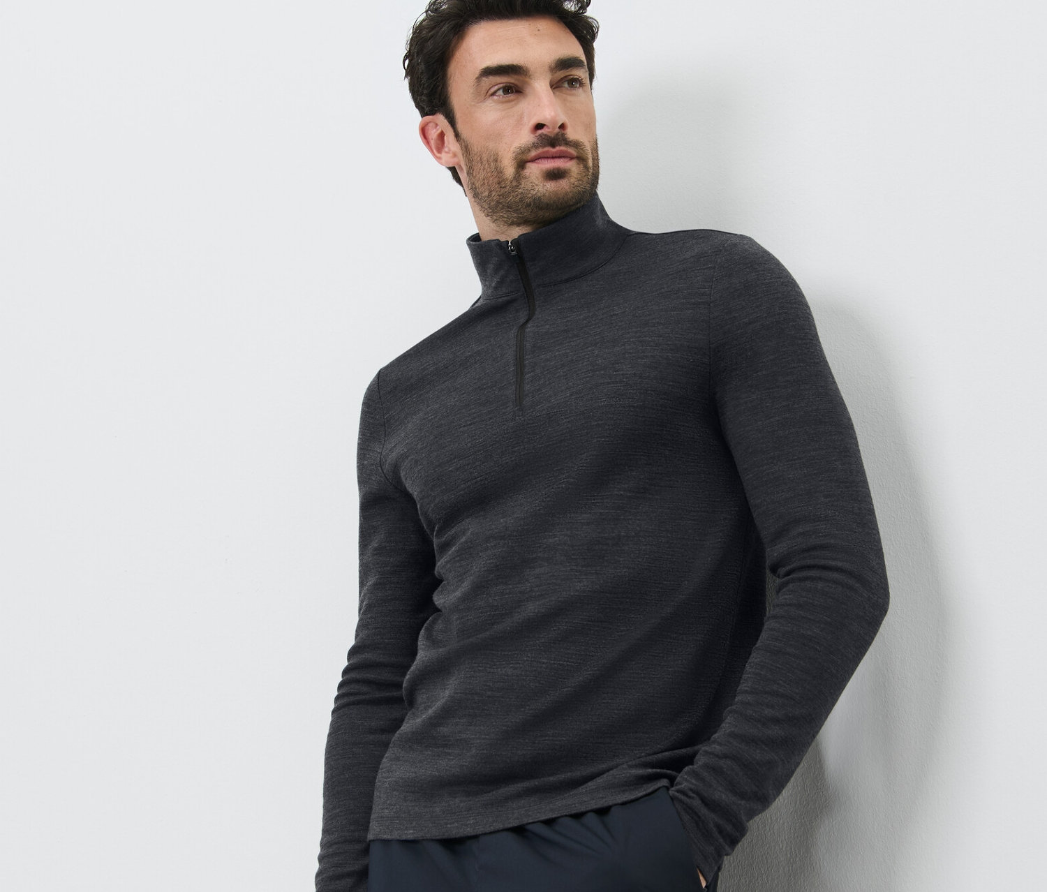 Un homme pose sur un fond blanc, portant un t-shirt technique avec de la laine certifiée RWS et un pantalon foncé.