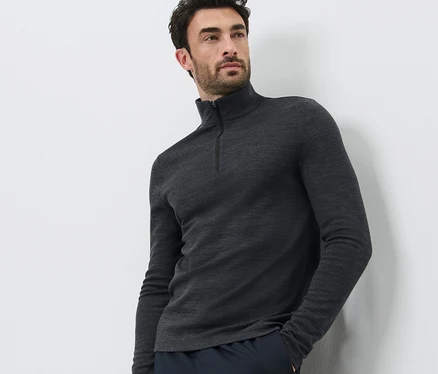Un homme pose sur un fond blanc, portant un t-shirt technique avec de la laine certifiée RWS et un pantalon foncé.