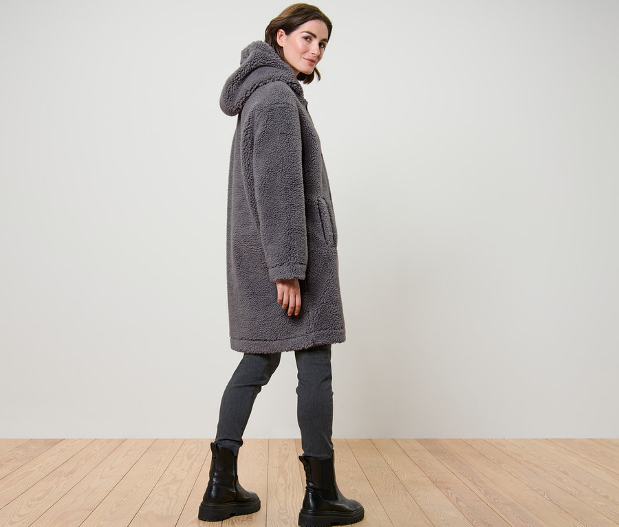 Femme posant dans un manteau en teddy gris avec capuche.